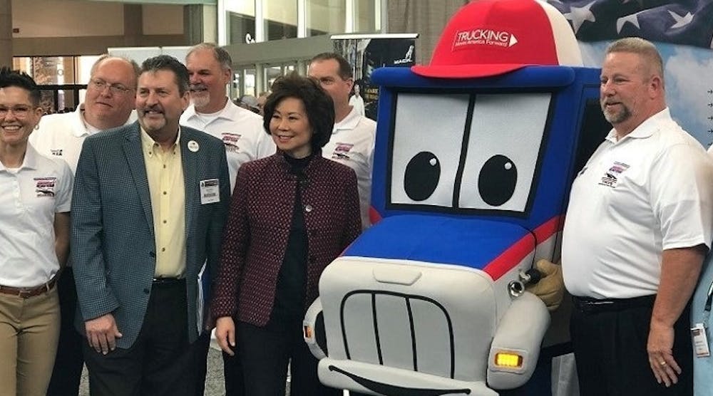 US Transportation Secretary Elaine Chao poses with Trucking Moves America Forward mascot Safety Sammy at the 2019 Mid-America Trucking Show.
