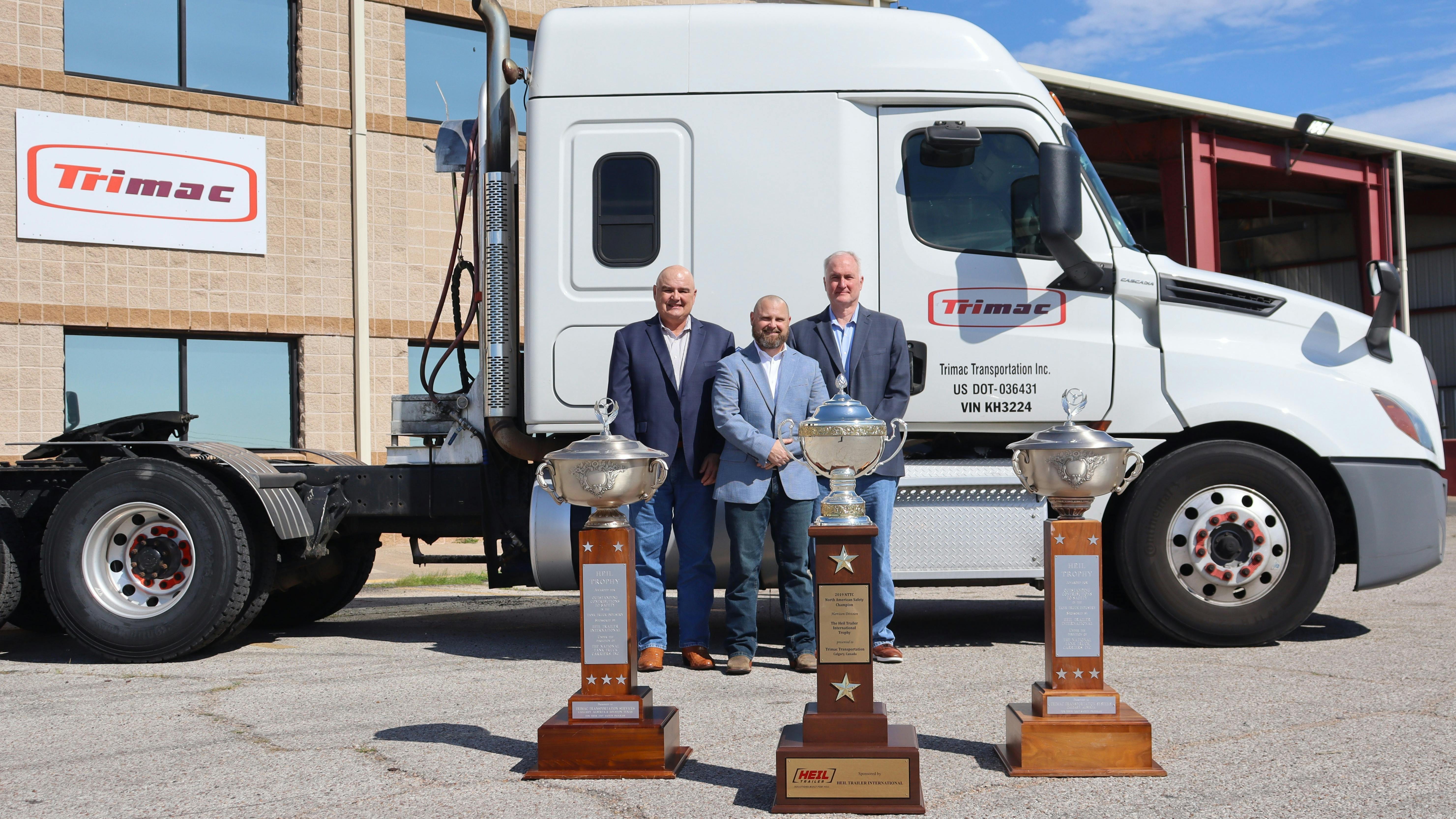 From left to right are Alex Guariento, Lance Hagler, and Bill Marchbank, who are standing behind Trimac's first three outstanding performance trophies outside the carrier's U.S. headquarters in the Houston area.