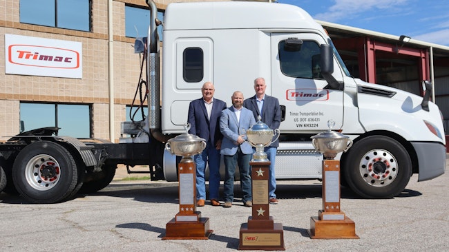 From left to right are Alex Guariento, Lance Hagler, and Bill Marchbank, who are standing behind Trimac's first three outstanding performance trophies outside the carrier's U.S. headquarters in the Houston area.