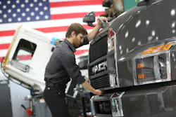 A technician performs maintenance on the front grille of a Mack truck inside a service facility. The manufacturer's new Premium Plus service contract is designed to streamline shop visits by bundling adaptive preventive care with comprehensive powertrain repair coverage.