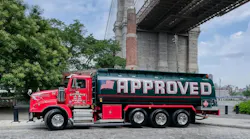A red and green Approved Oil tank truck parked on a cobblestone street under the Brooklyn Bridge in New York City.