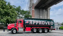 A red and green Approved Oil tank truck parked on a cobblestone street under the Brooklyn Bridge in New York City.